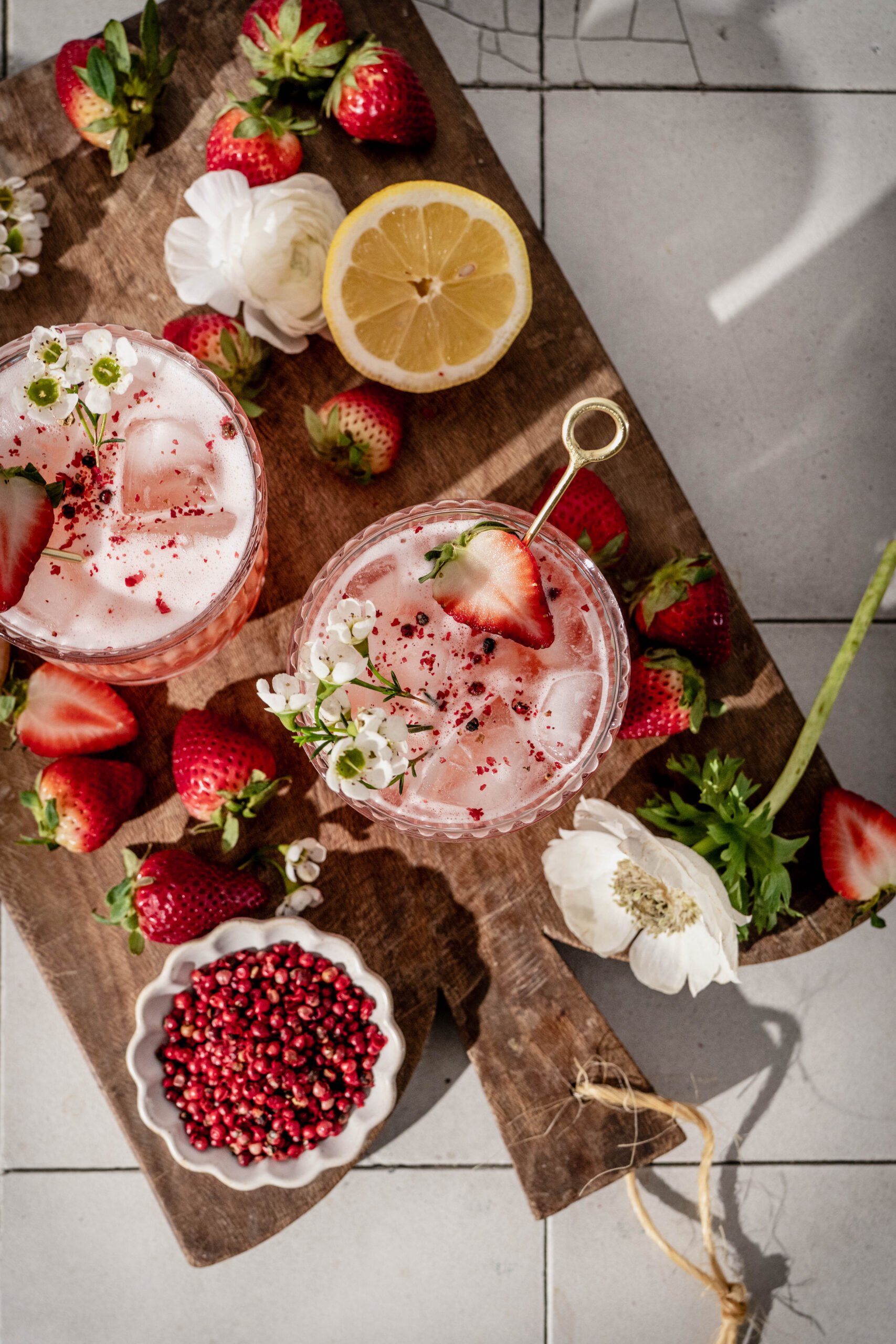 Sun kissed sipper a summer whiskey cocktail on a wood cutting board surrounded by fresh strawberries and flowers