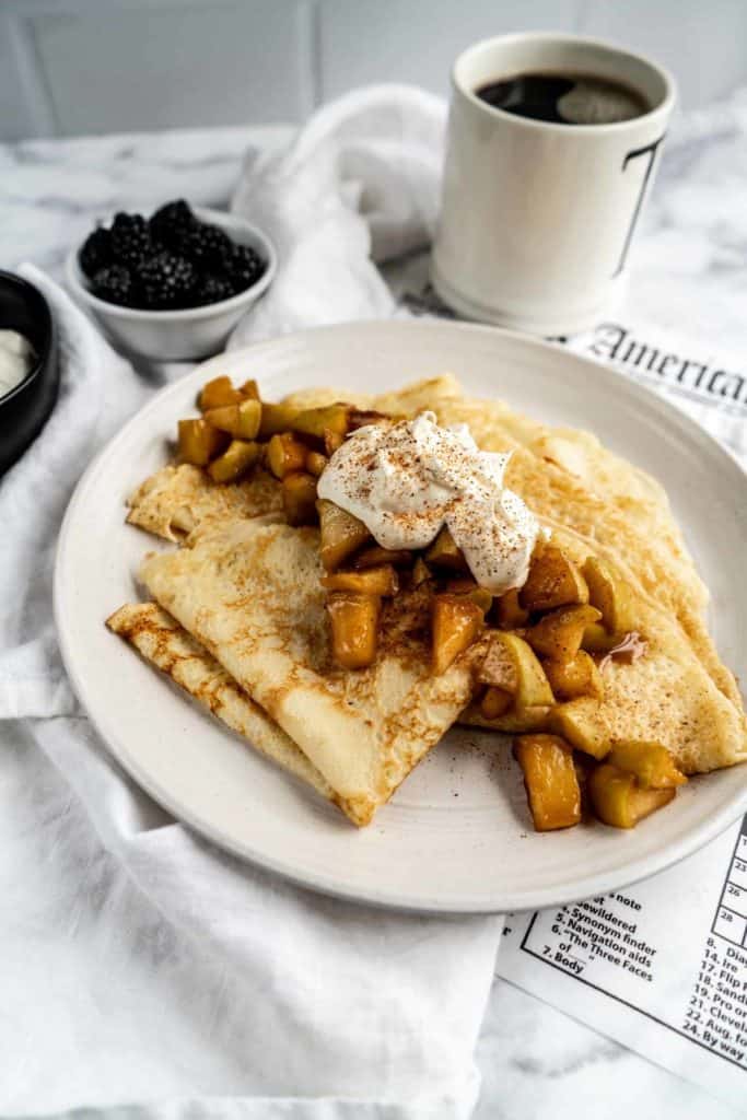 apple cinnamon crepes on plate with whipped cream served with coffee and fruit