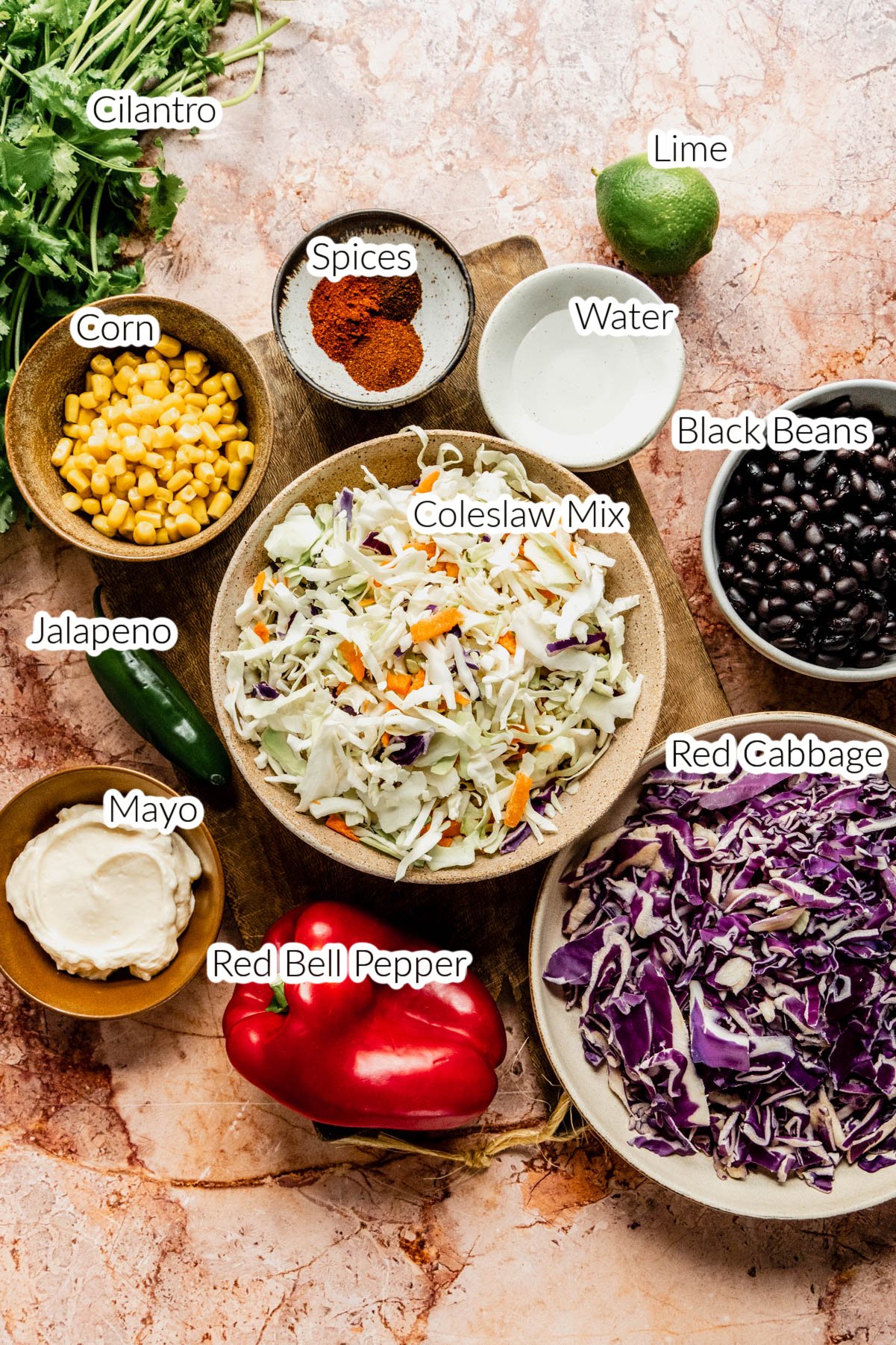 smoky summer slaw ingredients in bowls on brown marble background 