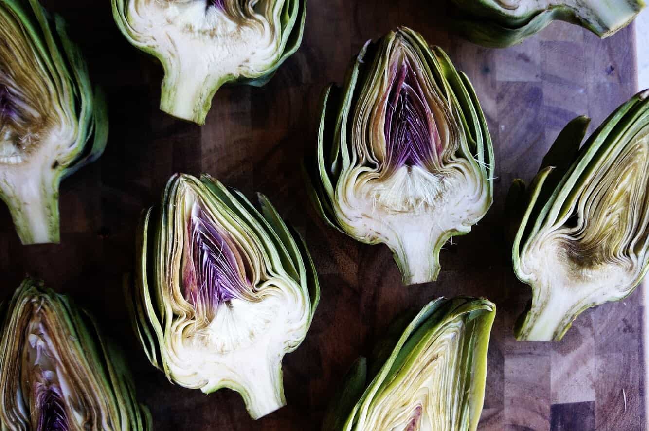 whole Artichokes cut in half on wood cutting board