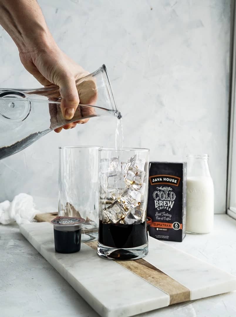 adding water to cold brew liquid pod in glass with ice