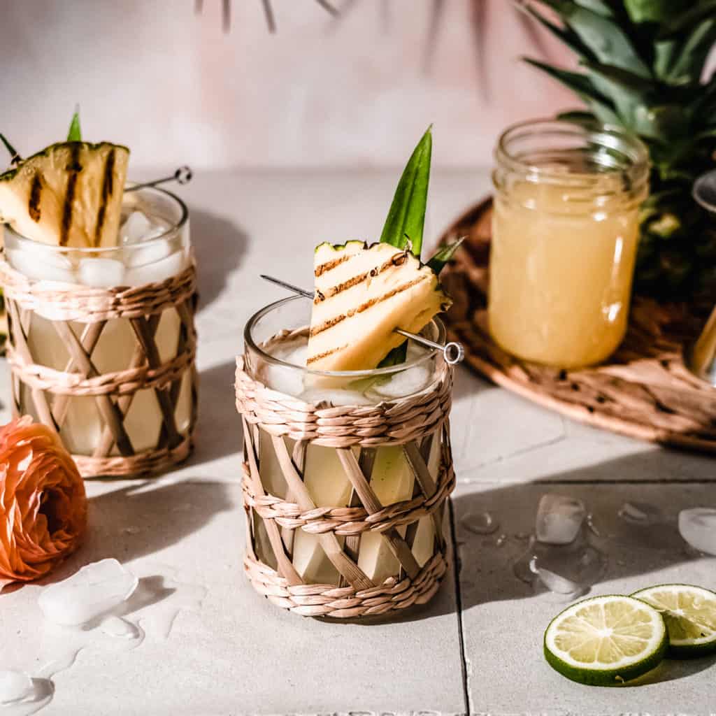 close up of pineapple moscow mule in highball glass with seagrass tumbler, garnished with grilled pineapple and pineapple leaves