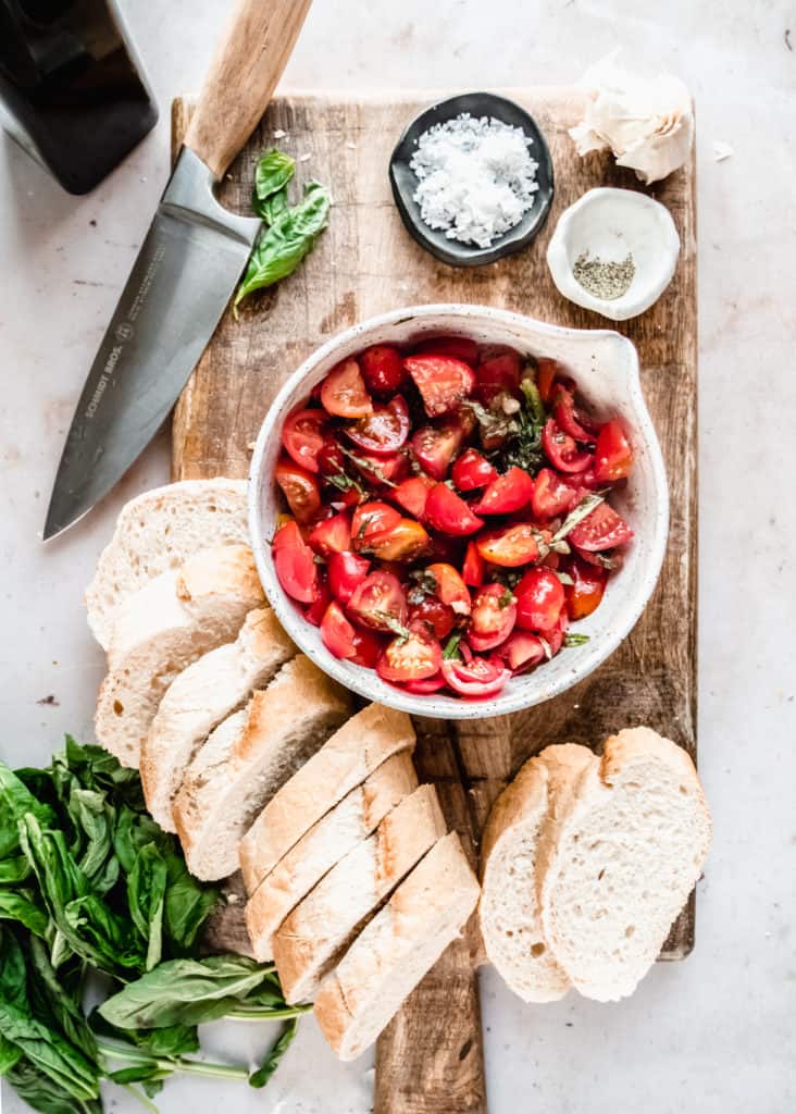 tomato basil mixture in bowl with slices of baguette on cutting board 