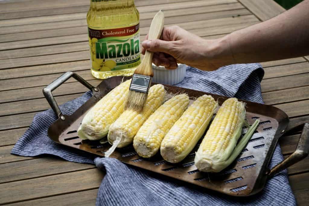 corn in husks being brushed with oil 