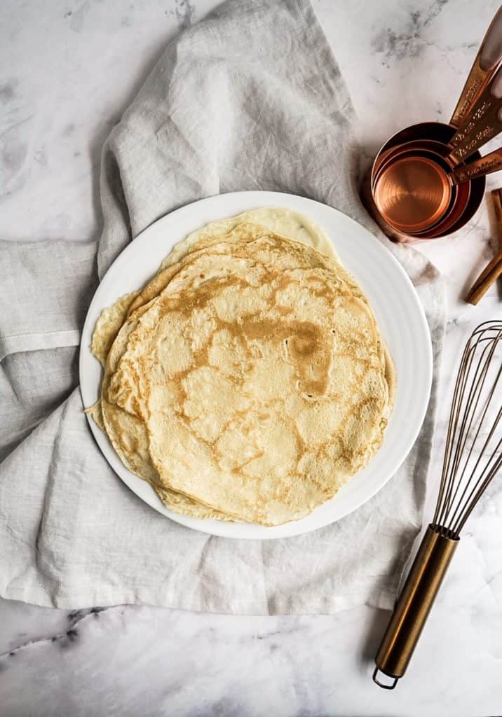 plain unfilled crepes on a plate next to a whisk 