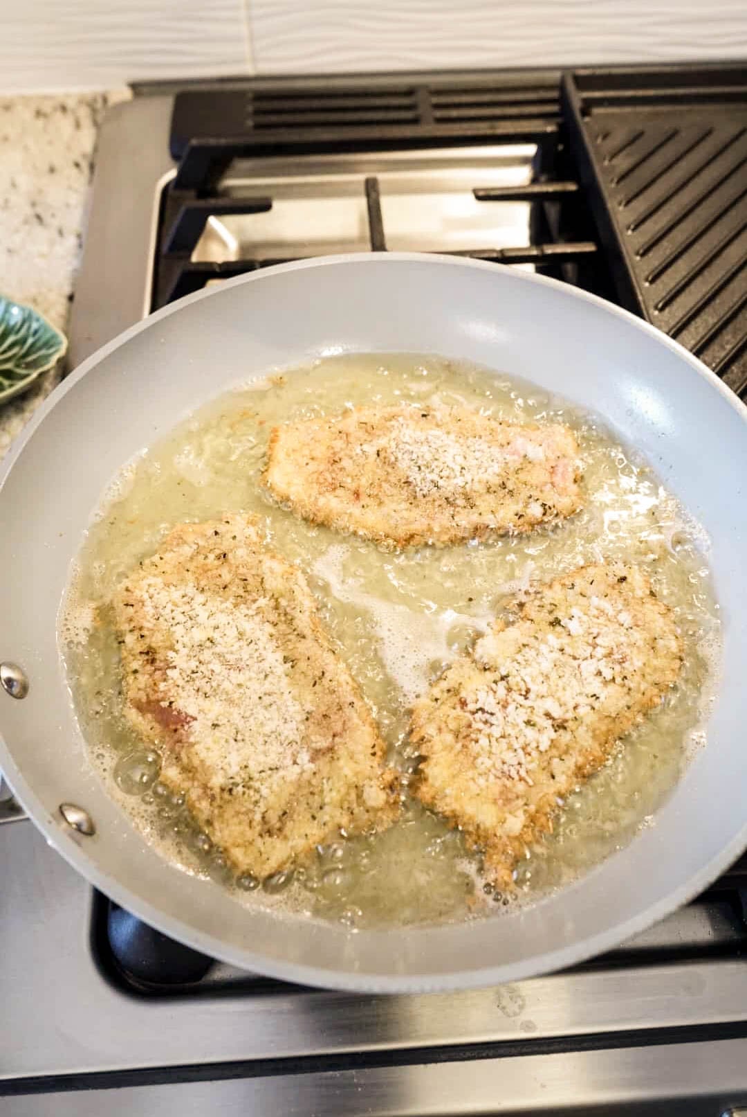 Breaded veal cutlets frying in a skillet with bubbling olive oil, turning golden and crispy before being served with Milanese sauce.