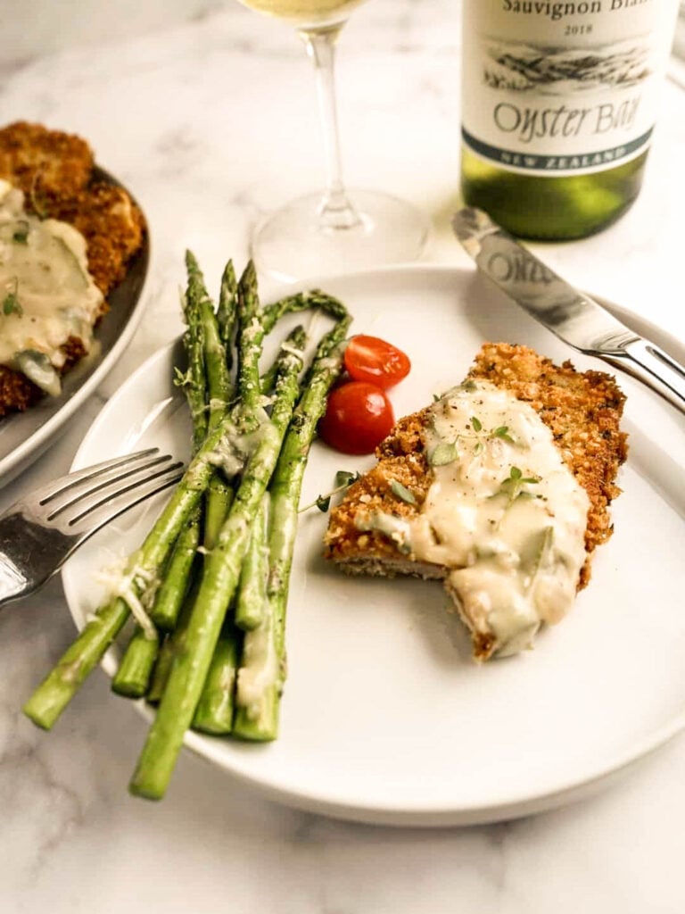 Crispy veal Milanese topped with creamy Milanese sauce served with roasted asparagus and cherry tomatoes, paired with a glass of white wine.