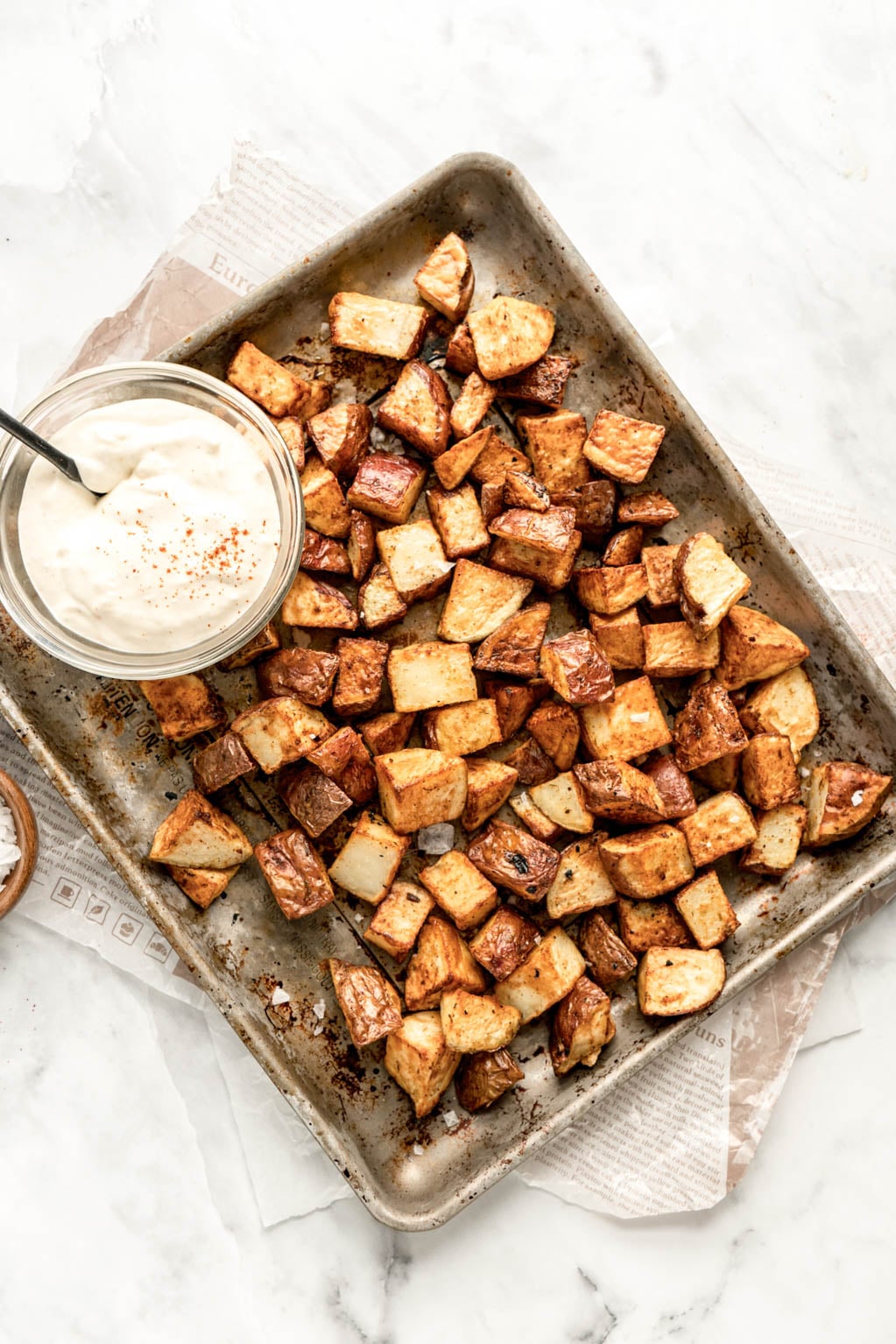 Overhead view of crispy golden air fryer cubed potatoes on a baking sheet, served with a bowl of creamy truffle aioli sprinkled with paprika for dipping.