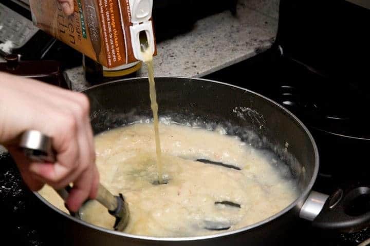 Chicken stock for piccata sauce being poured into saute pan on stove.