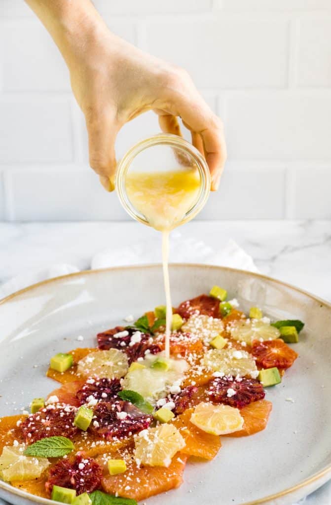 dressing being poured over citrus salad
