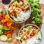 **Alt text:** *Overhead view of two bowls of healthy cashew chicken with white rice, cashews, red bell peppers, sugar snap peas, pineapple, and fresh cilantro on a wooden cutting board.*