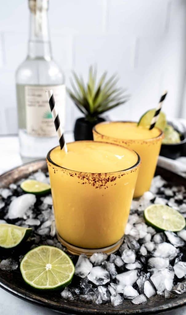 mango ginger margarita on drink tray with ice and limes