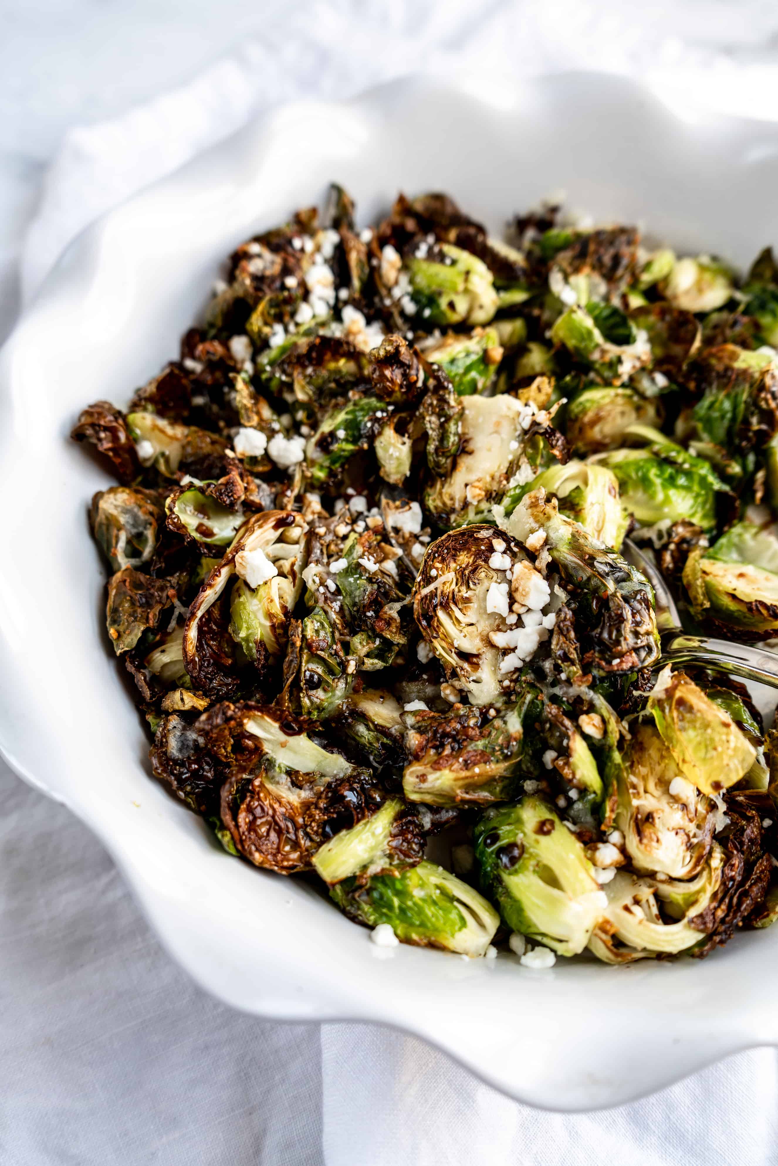 close up of balsamic-roasted brussels sprouts in baking dish sprinkled with goat cheese and balsamic glaze 