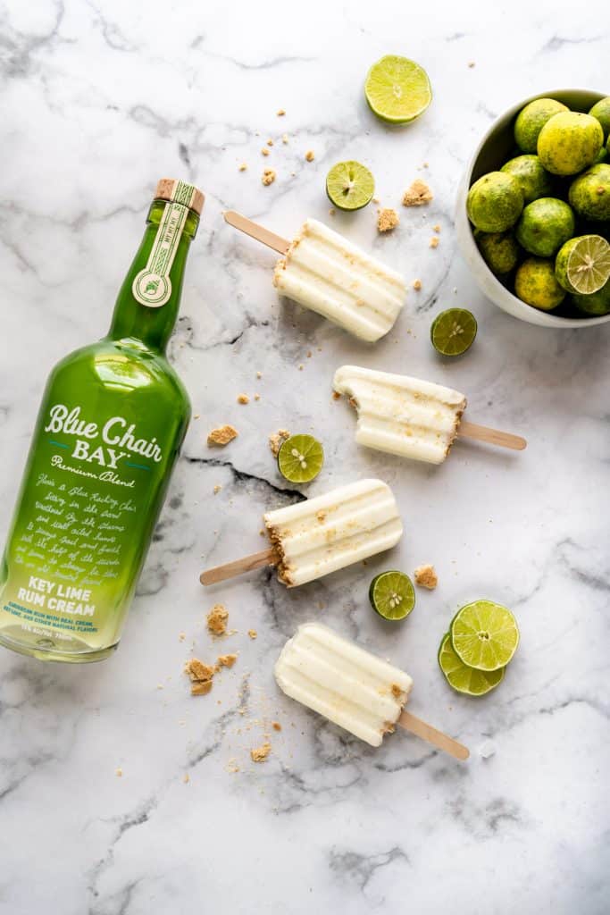 key lime popsicles laying on countertop with bottle of rum
