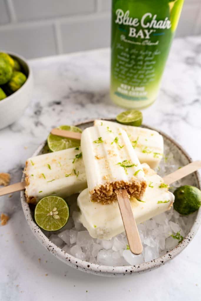 key lime popsicles stacked in bowl with limes and ice