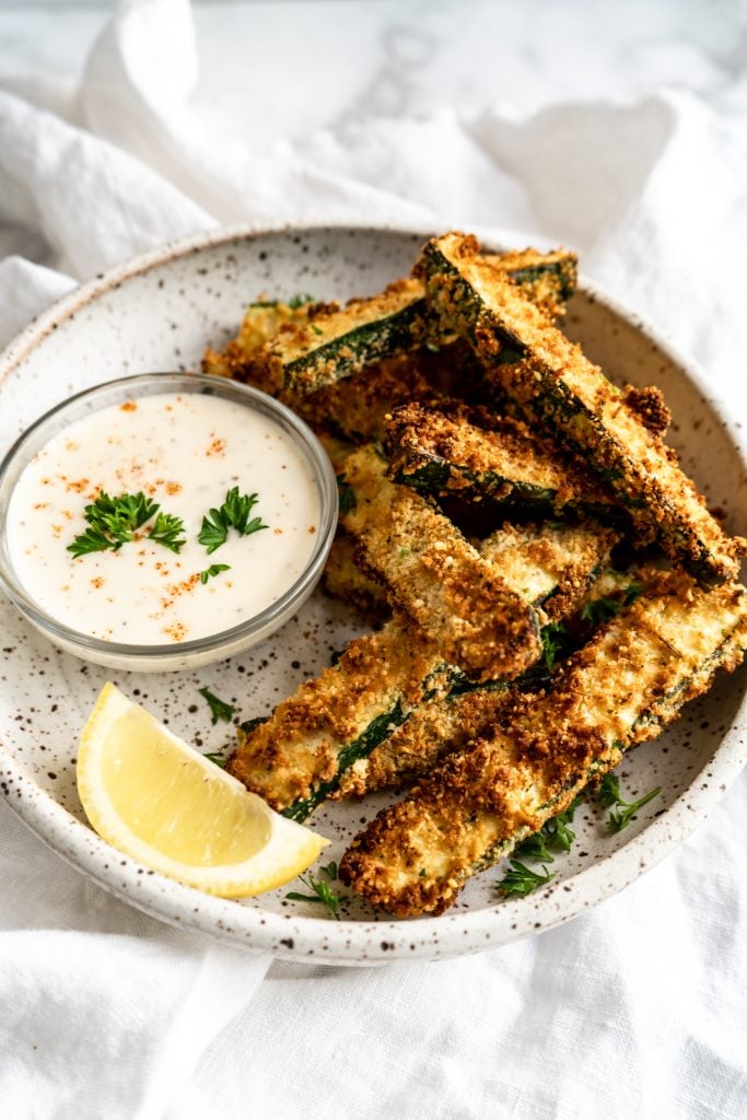 zucchini fries in bowl with dipping sauce and lemon wedge