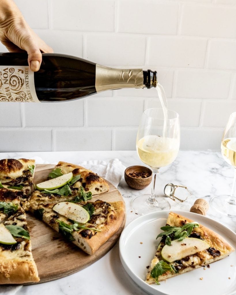 Gruyère and Caramelized Onion pizza sliced on cutting board with a hand pouring wine into glass