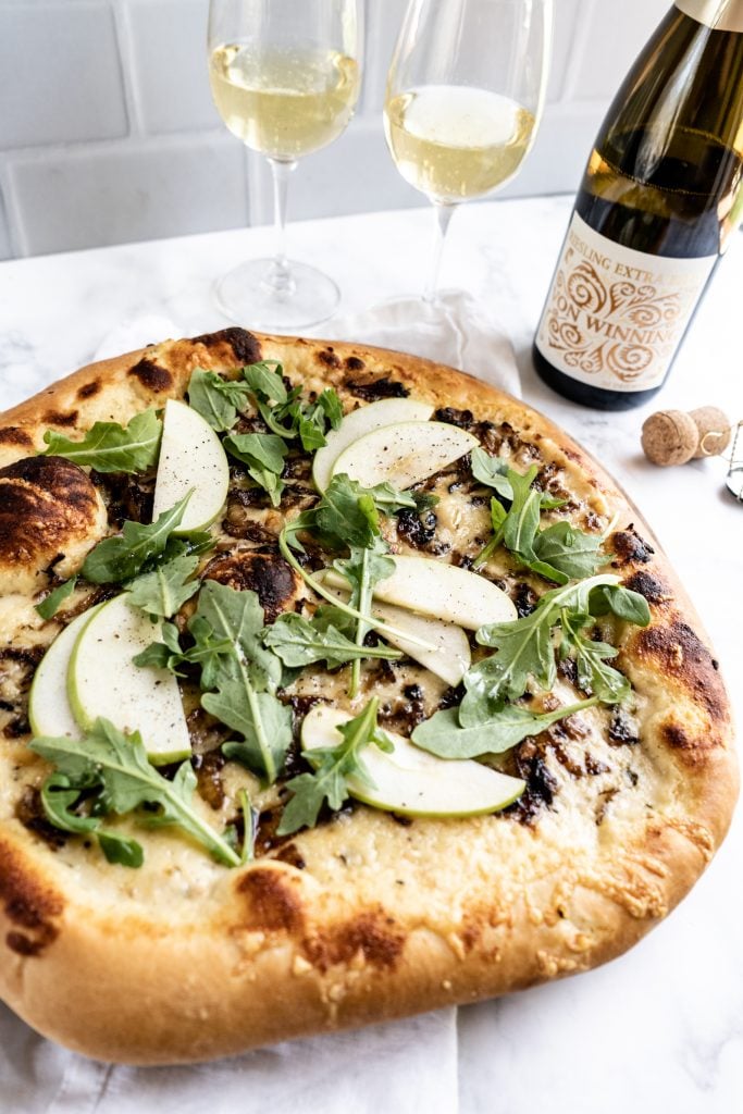 Gruyère and Caramelized Onion pizza on cutting board with two glasses of wine behind