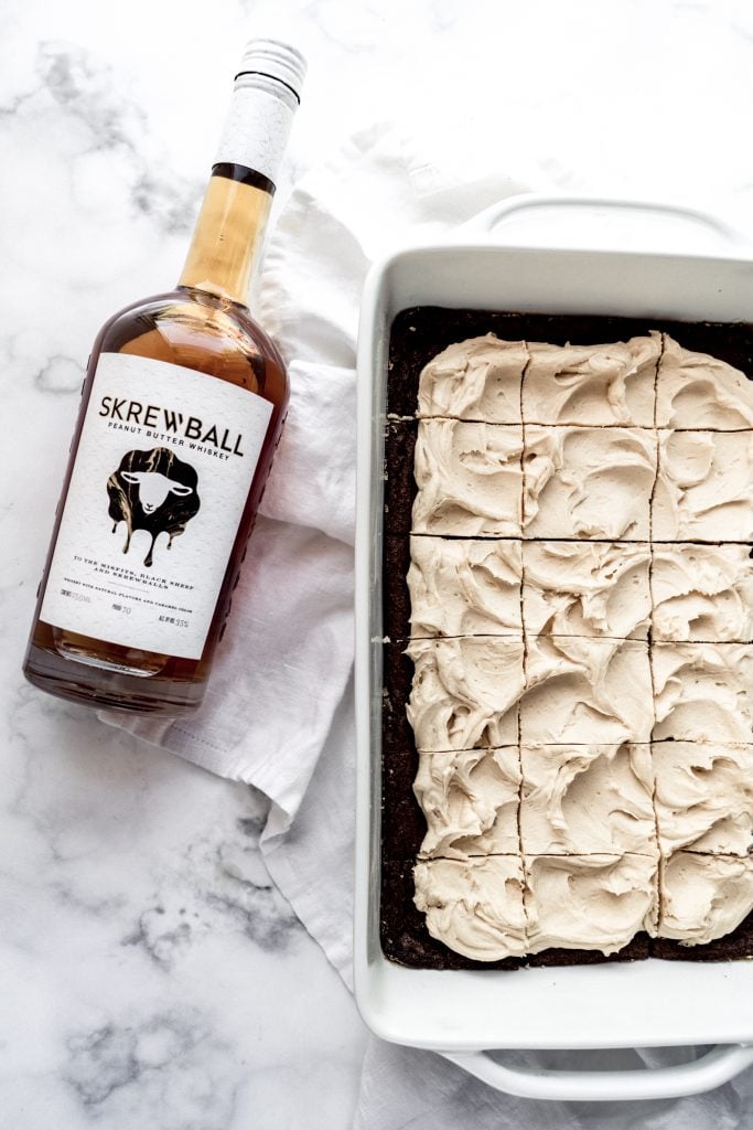 whiskey brownies in pan frosted and sliced with bottle of whiskey laying beside the pan