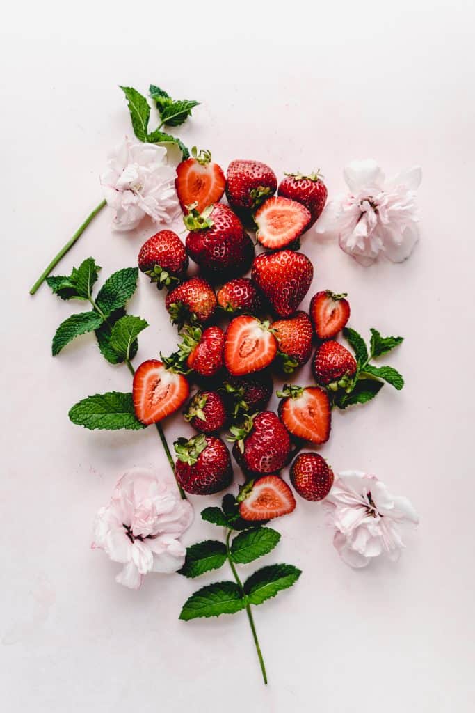 strawberries sliced and whole on pink backdrop with pink flowers and mint