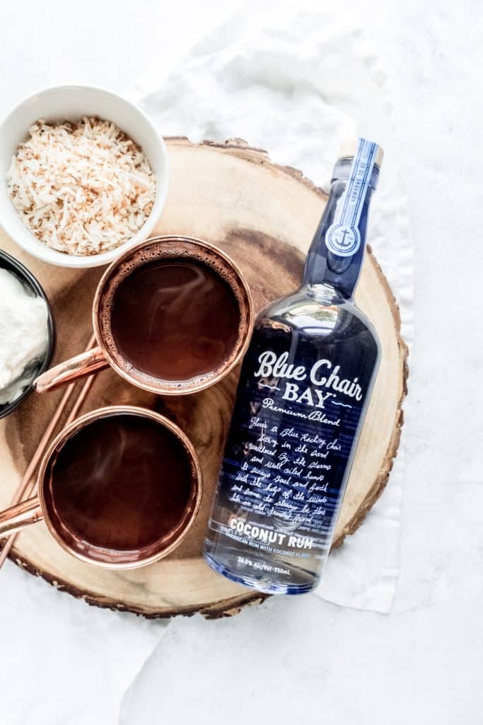 boozy coconut hot chocolate ingredients on wood slab, hot chocolate in cups