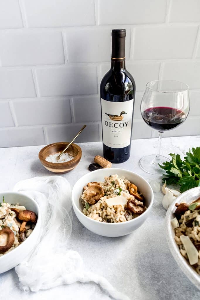 Instant pot Mushroom Gorgonzola risotto in bowl with wine glass and bottle behind