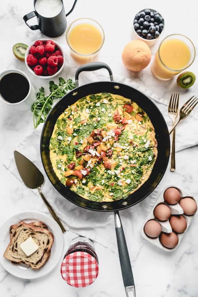 spinach and red pepper frittata on breakfast table with orange juice and fruit