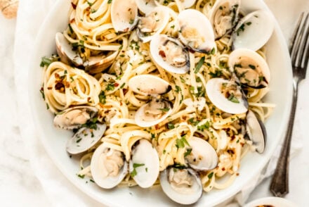 Overhead view of linguine with clams in white wine sauce, featuring tender pasta and opened clams tossed with garlic, olive oil, and lemon, finished with fresh parsley and red pepper flakes on a white linen backdrop.