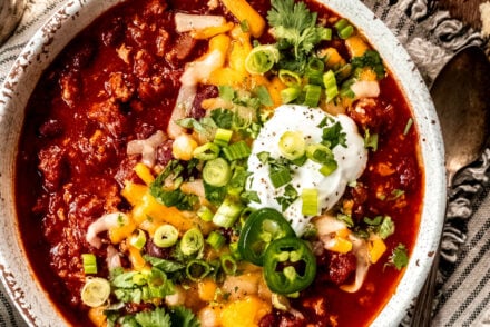 Turkey chili garnished with shredded cheese, cilantro, green onion and sour cream in a white bowl with a striped napkin underneath.