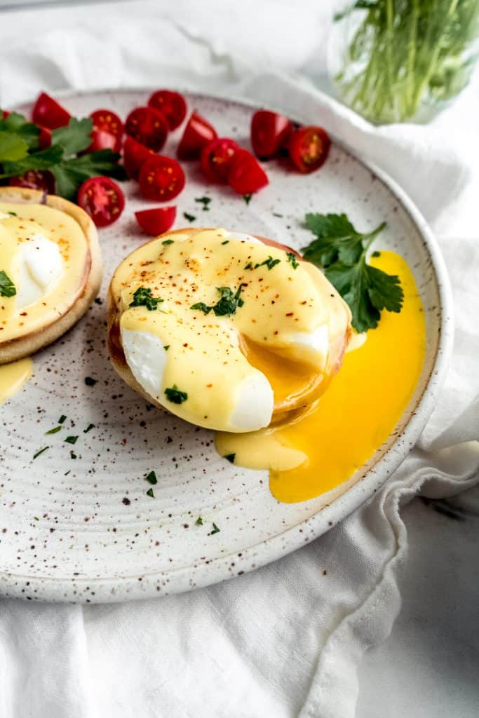 eggs benedict with citrus hollandaise with egg yolk spilling out on plate 