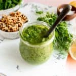 pea shoot pesto in a jar with walnuts and raw pea shoots surrounding it