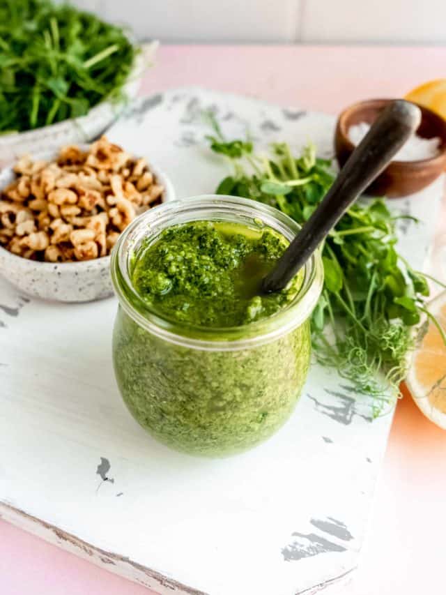 pea shoot pesto in a jar with walnuts and raw pea shoots surrounding it