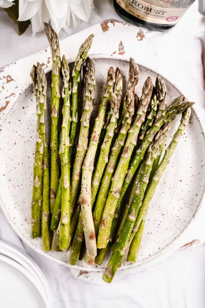 raw asparagus on plate with olive oil and salt and pepper