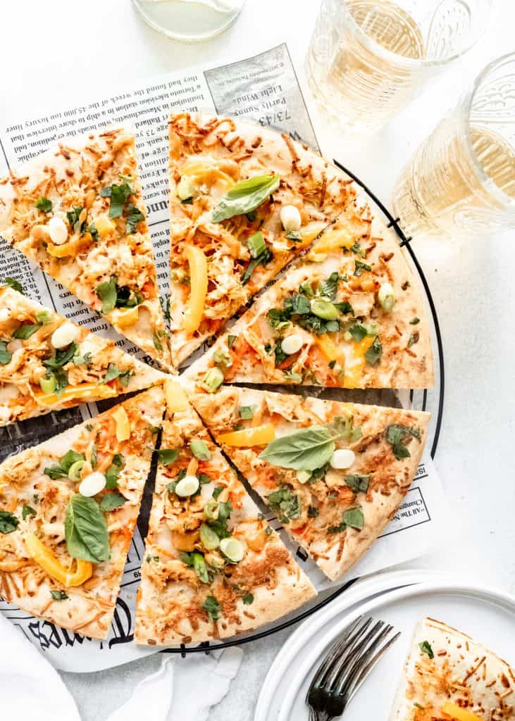 thai chicken pizza sliced on cooling rack with wine glasses