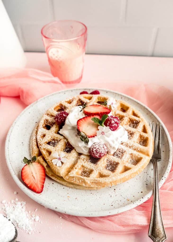 yeast Belgian waffles topped with  whipped cream and strawberries on plate 