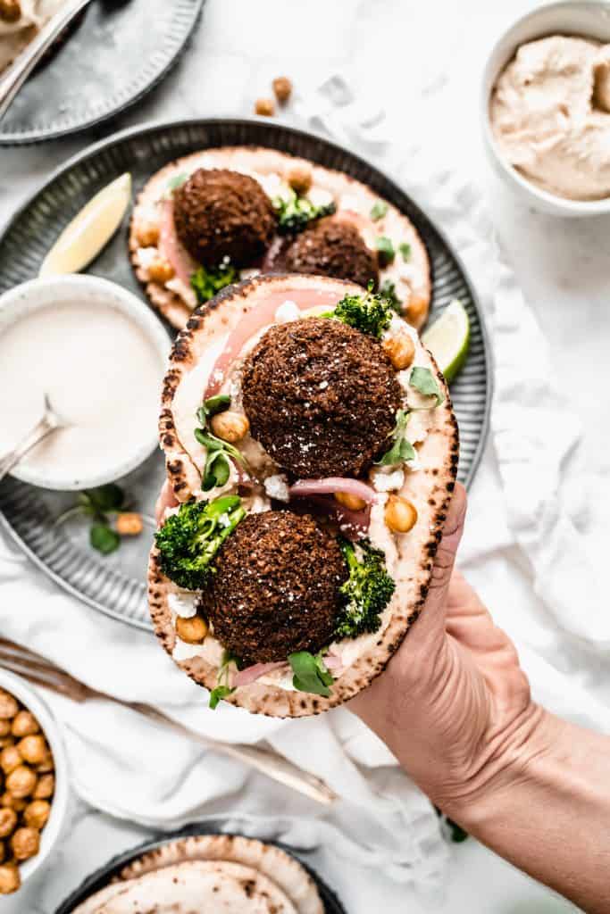 hand holding sweet potato falafel in pita wrap with toppings 