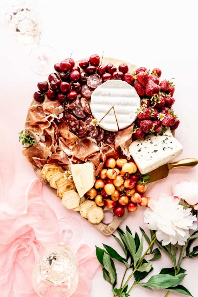 overhead shot of summer charcuterie board with wine glasses and peonies