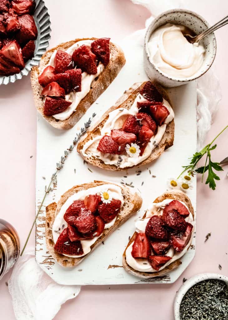 roasted strawberry bruschetta on white cutting board with white flowers