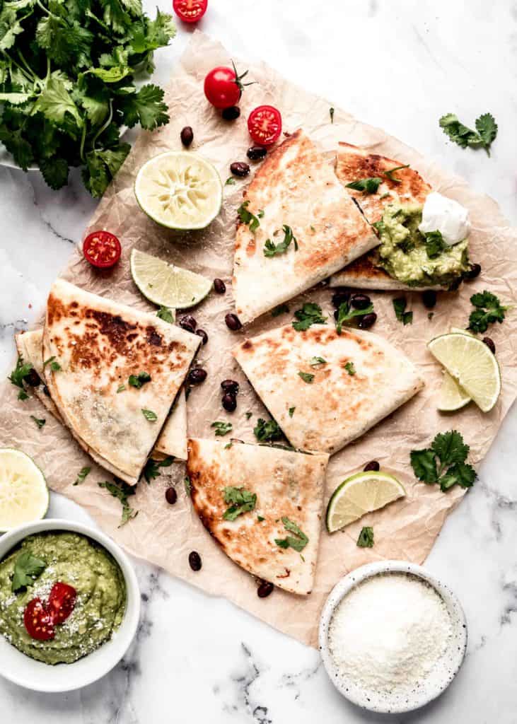 quesadillas on parchment paper garnished with guacamole and sour cream 