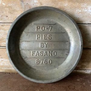 Metal pie plate with "Pies by Fasano" inscribed on a wooden background