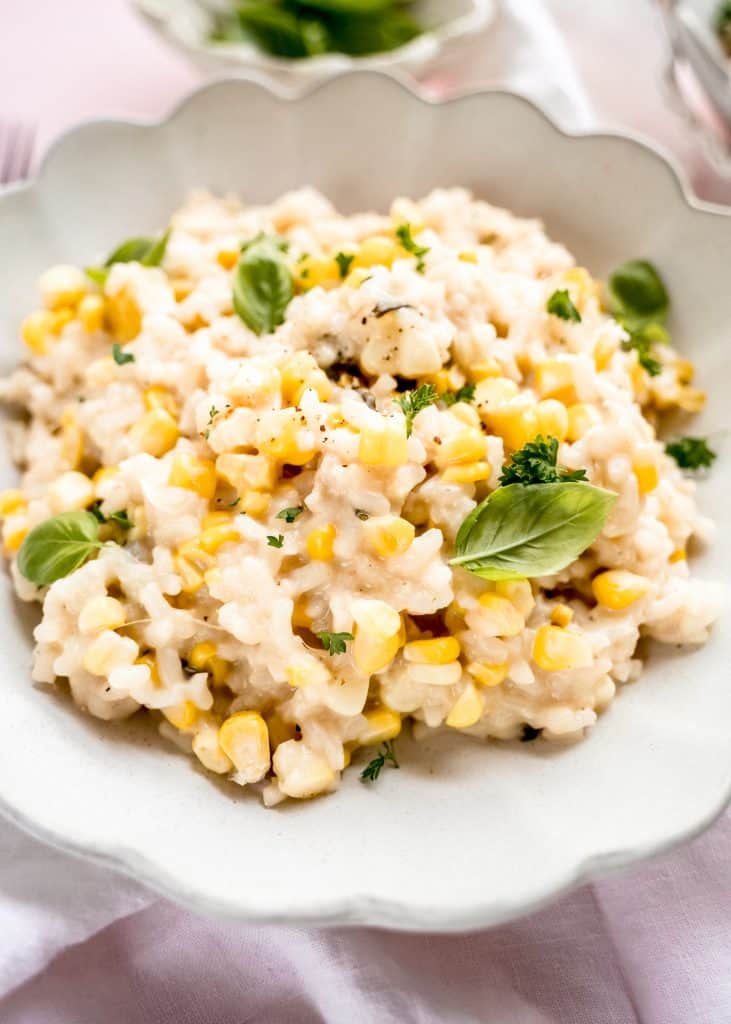 close up shot of sweet corn risotto in bowl garnished with basil 