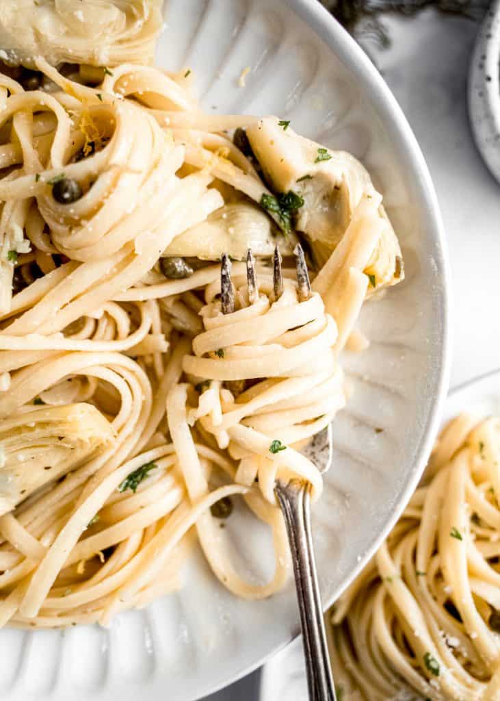 lemon artichoke pasta on plate with noodles twirled around fork.