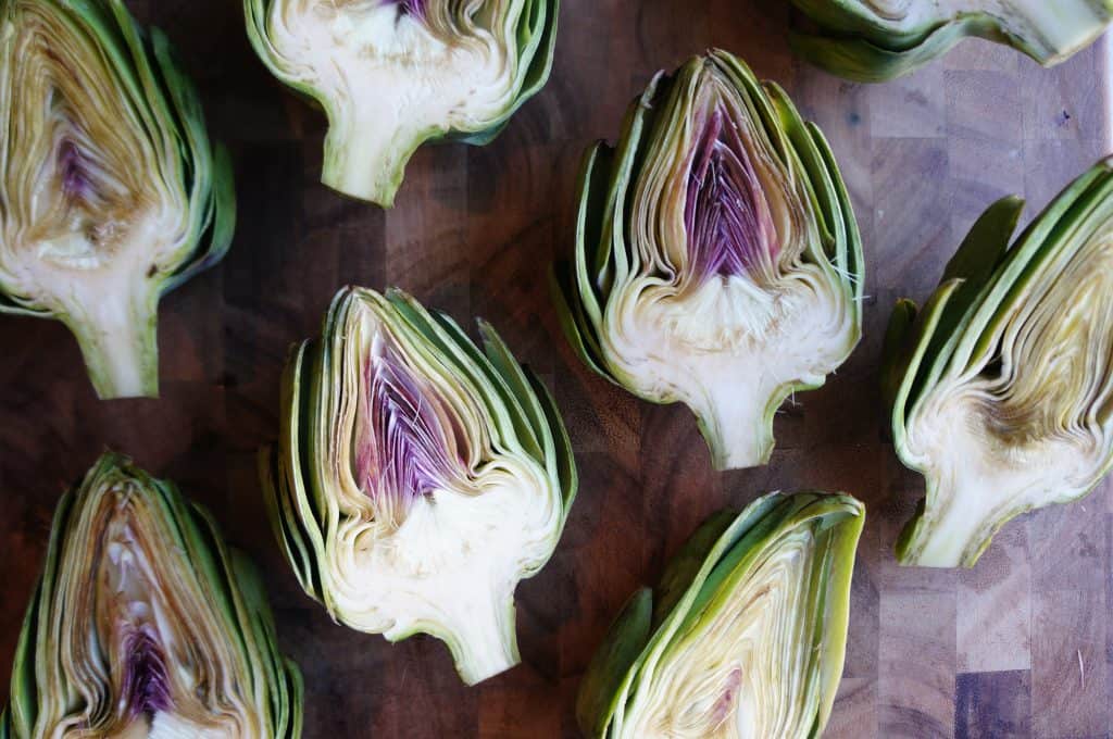 raw artichokes sliced in half cut side up on cutting board