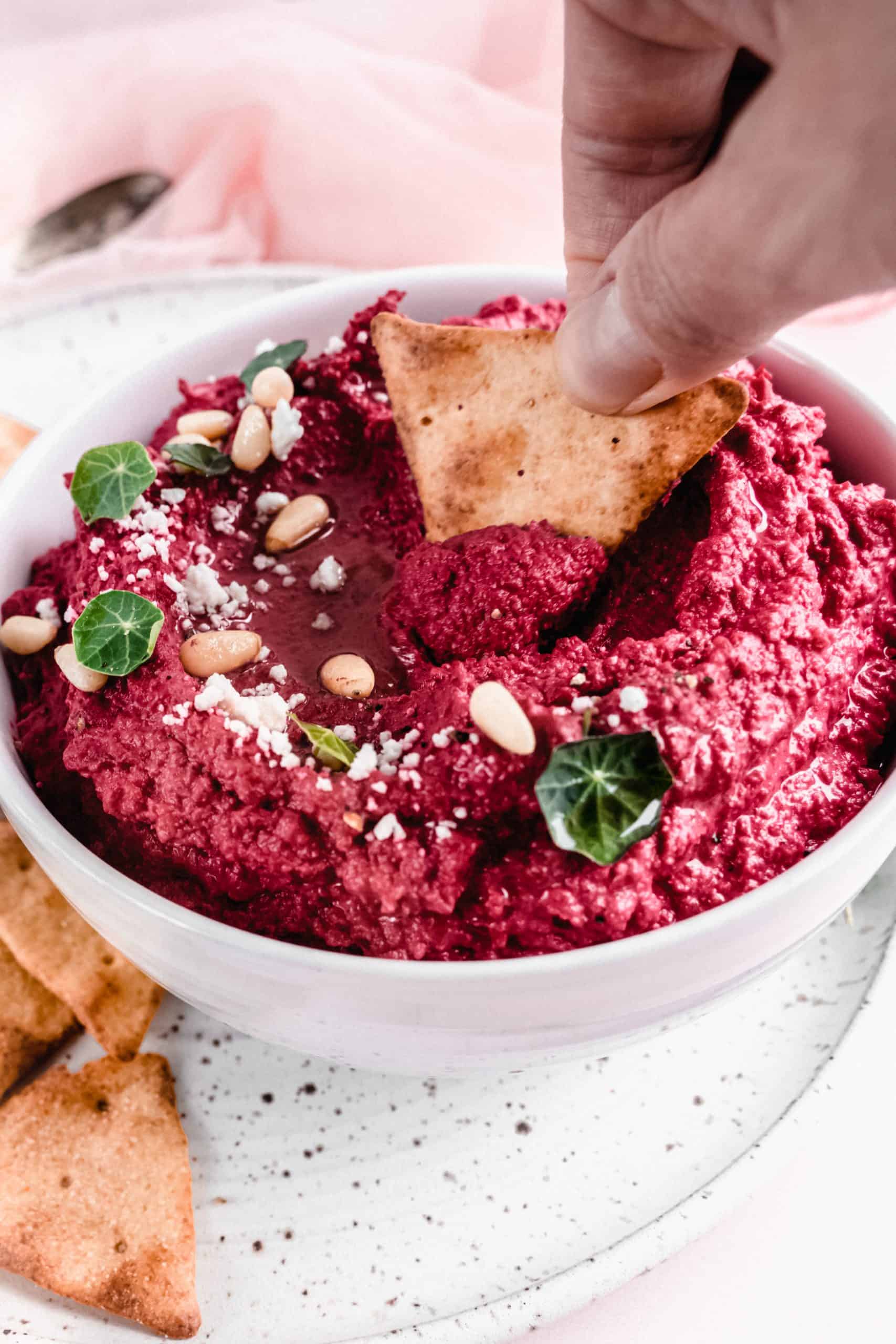 close up side shot of beet hummus garnished with feta cheese and pine nuts and greens