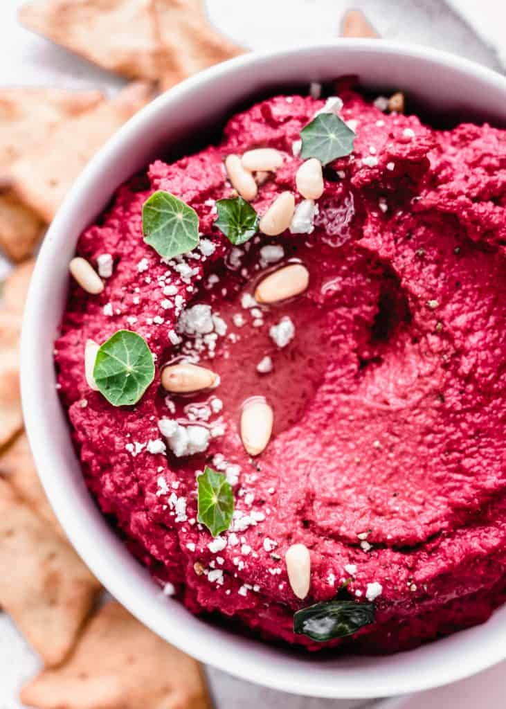 overhead shot of beet hummus garnished with goat cheese and pine nuts and greens with pita chips on plate