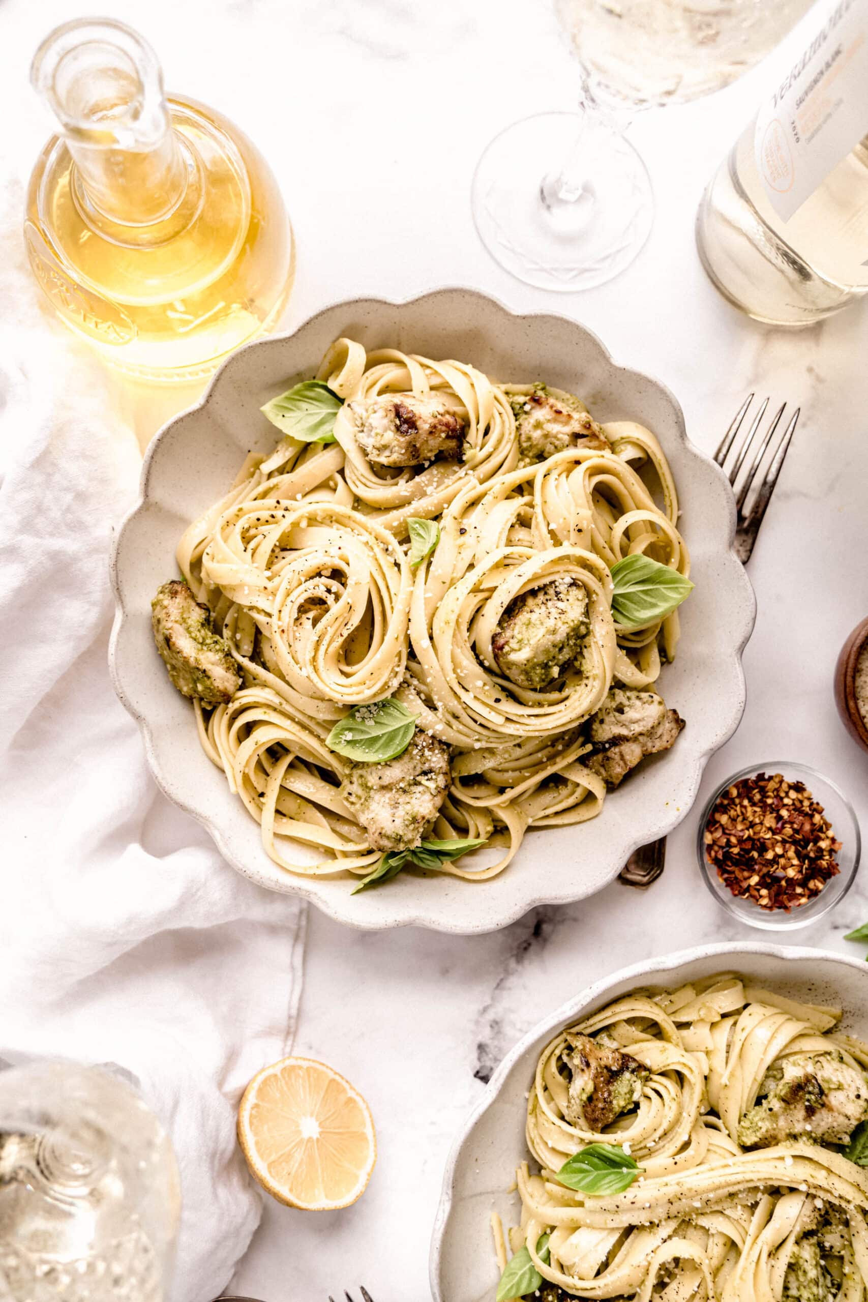 Overhead view of chicken pasta pesto with tender chicken pieces and long pasta tossed in basil pesto, garnished with fresh basil and parmesan on a light marble surface.