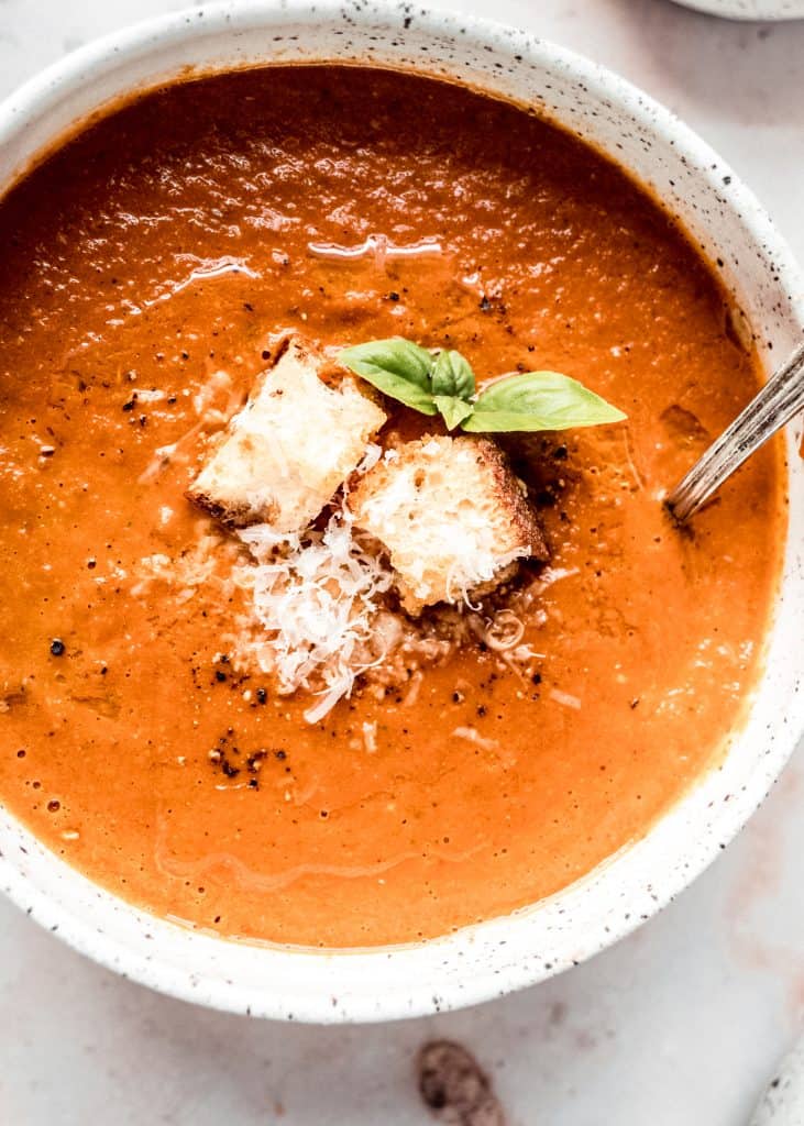 close up shot of roasted tomato soup in bowl garnished with basil, pepper and parmesan croutons