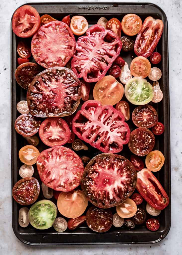 raw heirloom tomatoes sliced in half on sheet pan 