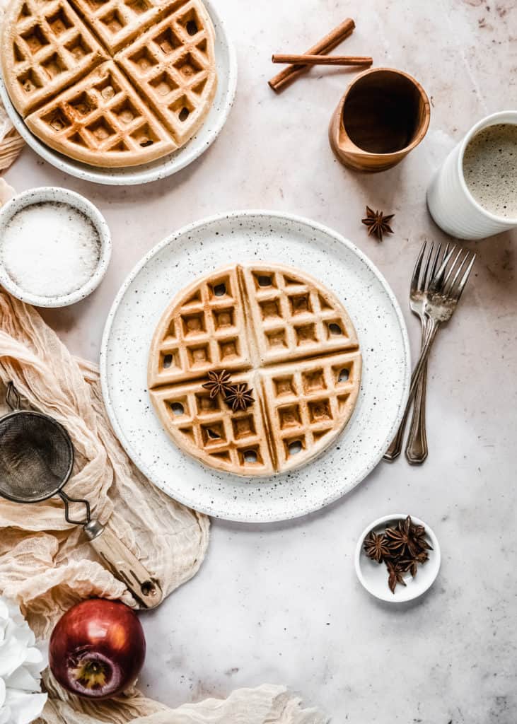 apple butter waffles on plate next to cup of coffee and maple syrup in wood cup