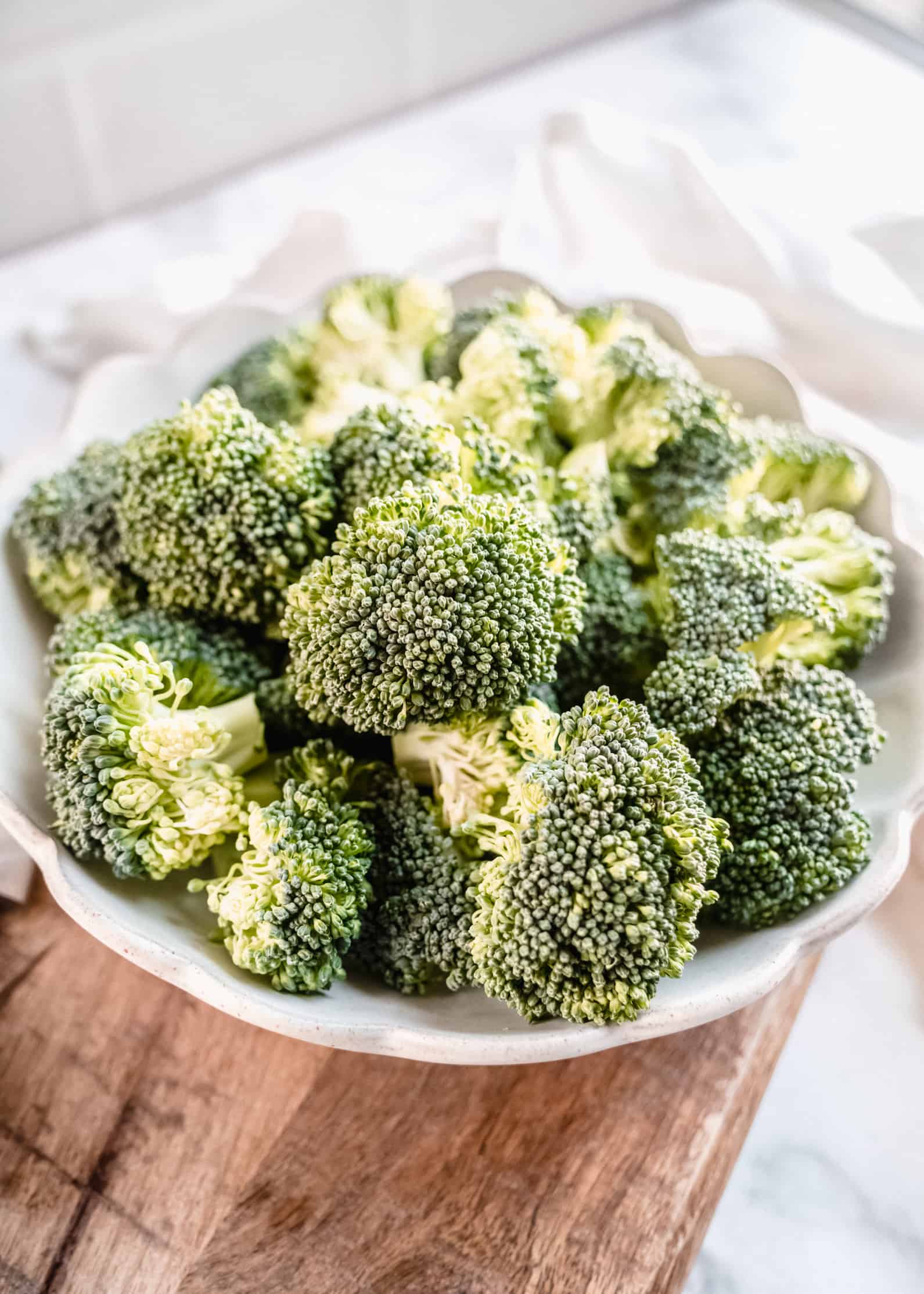 raw broccoli florets in a bowl on cutting board
